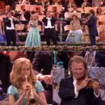 As André Rieu begins Sous Le Ciel De Paris, the entire audience is swept into a dream. The stage glows softly, echoing the charm of Parisian nights, while the orchestra brings every cobblestone and streetlight of the City of Love to life. Eyes glisten, couples lean into each other, and a quiet wave of emotion rolls through the hall. Some smile in bittersweet remembrance, others sit in awe, visibly moved. With every note, Rieu doesn’t just perform—he transports. This is more than music; it’s a breathtaking tribute to love, longing, and the magic of Paris under the stars.